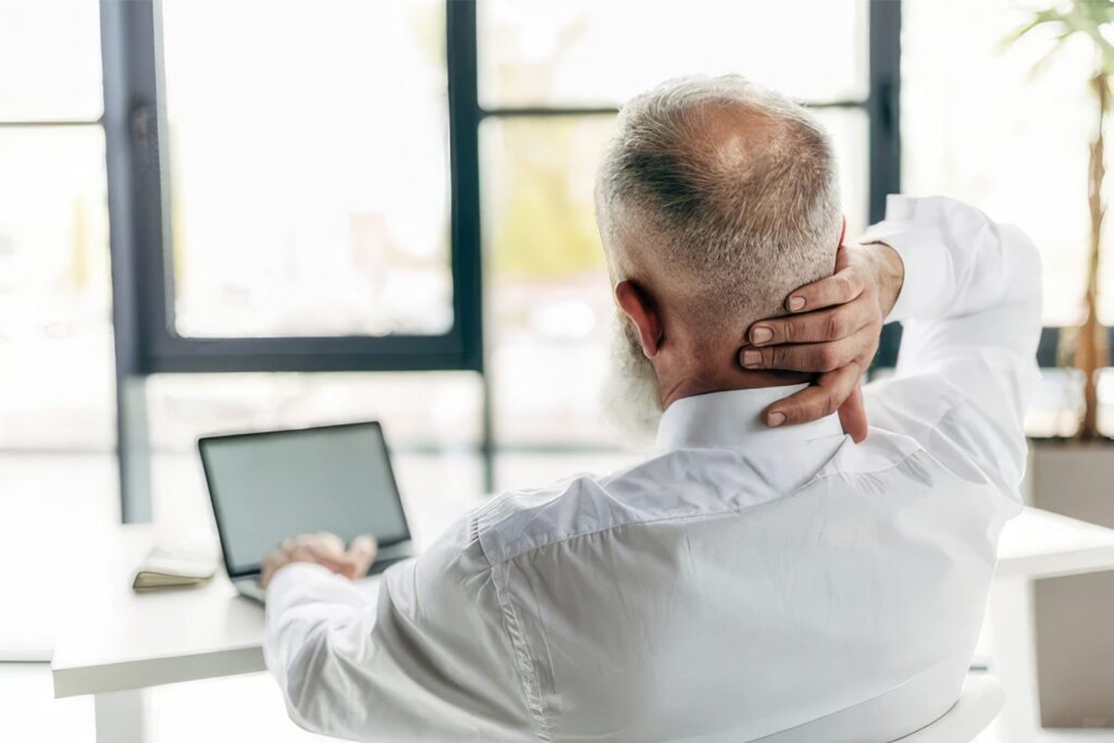 Person sitting at a desk with a stiff neck and tight shoulders
